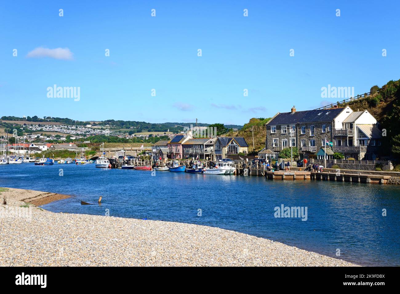 Fishing boats and yachts moored along the River Axe in the harbour with buildings and countryside to the rear, Axmouth, Devon, UK. Stock Photo