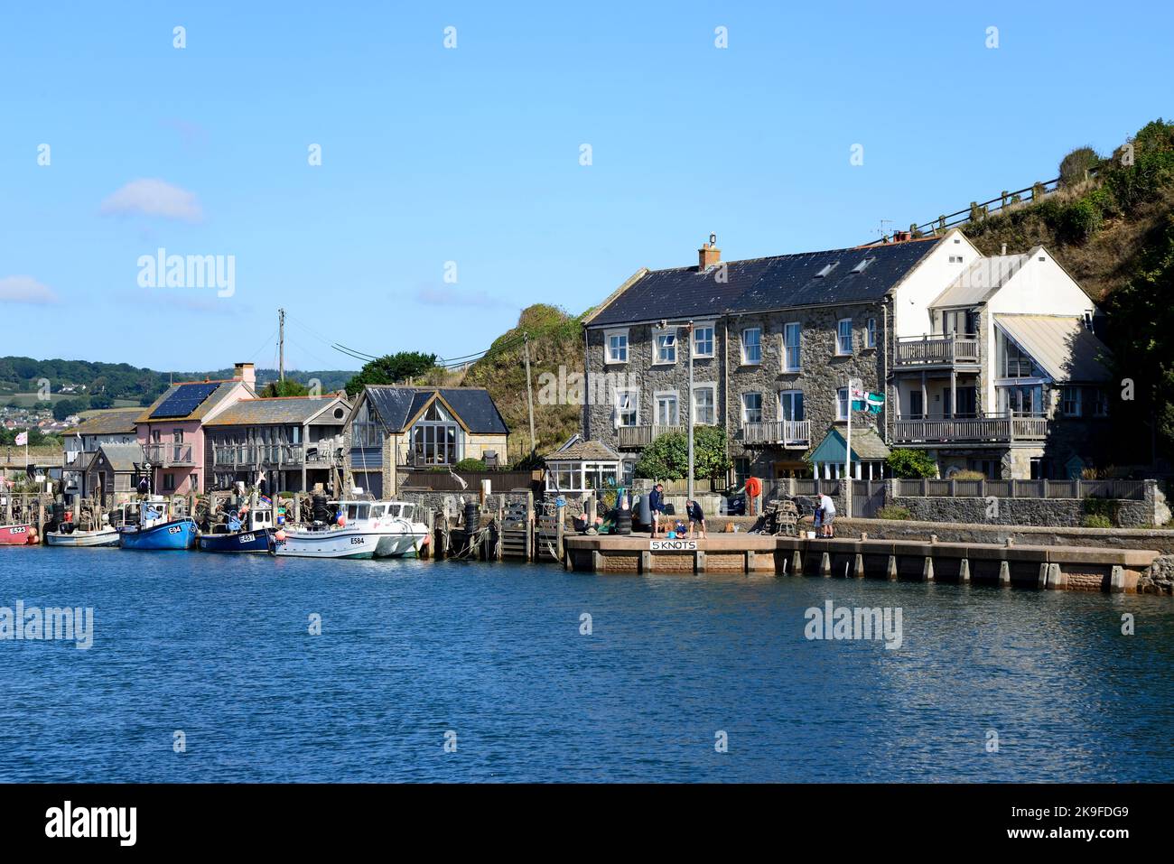 Boats moored along the waterfront along the River Axe with waterfront buildings to the rear, Axmouth, Devon, UK, Europe. Stock Photo