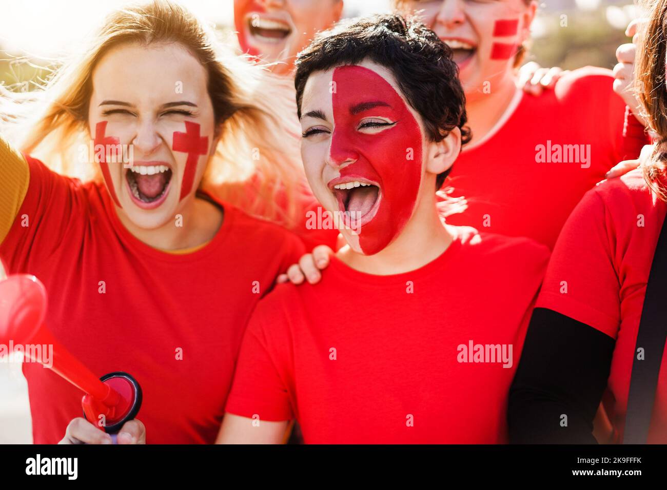 Red sport fans screaming while supporting their team - Football supporters having fun at competition event - Focus on center girl face Stock Photo