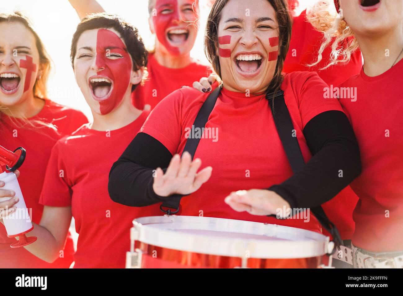 Red sport fans screaming while supporting their team - Football supporters having fun at competition event - Focus on girl playing drums Stock Photo