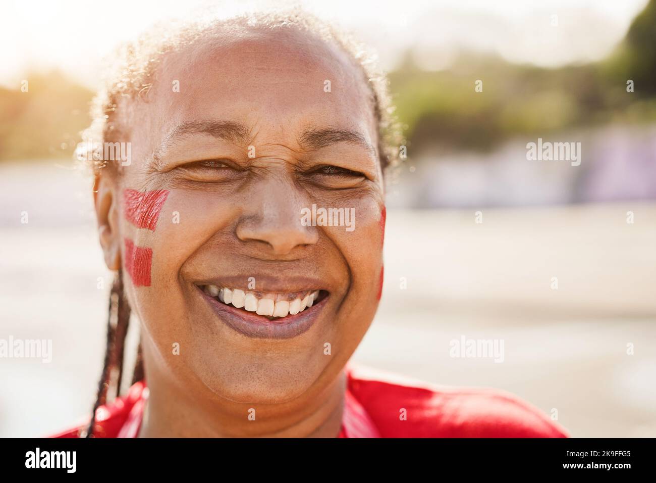 Red african senior sport fan laughing out of the stadium before football match - Focus on face Stock Photo