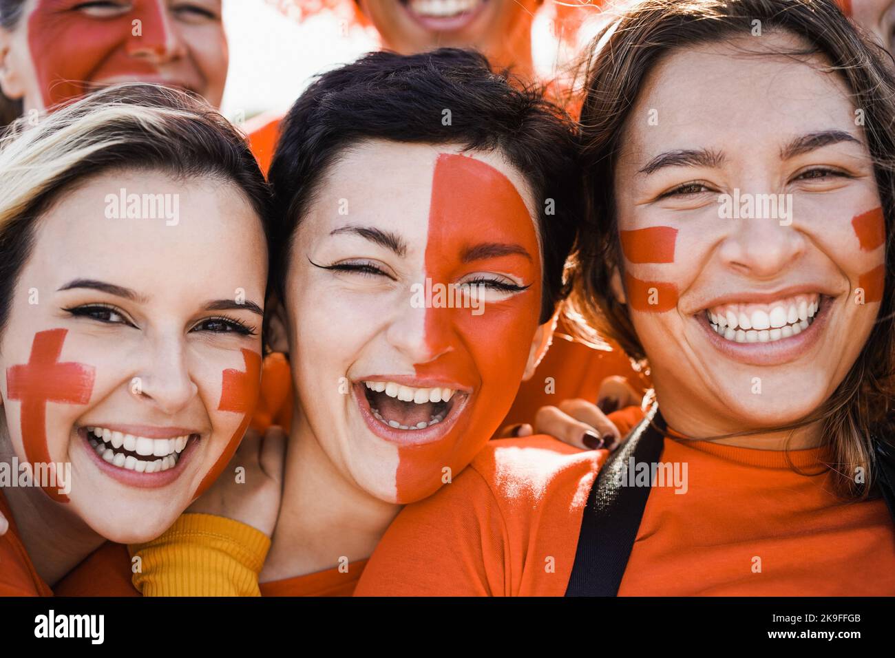 Orange sport fans having fun supporting their team - Football supporters having fun at competition event - Focus on left girl eye Stock Photo