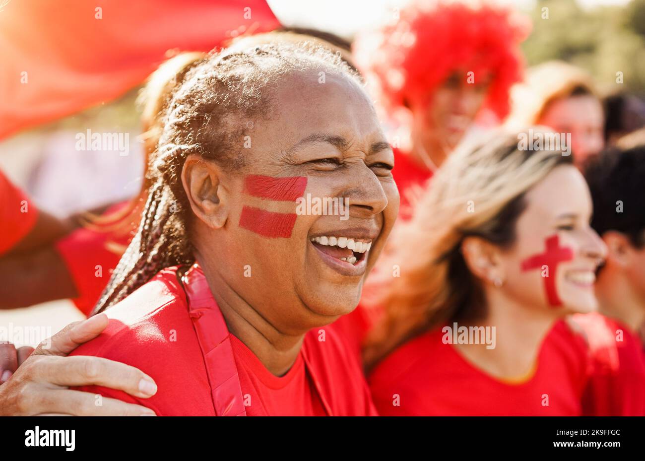 African senior red sport fan supporting their team - Multiracial football supporters having fun at competition event - Focus on woman face Stock Photo
