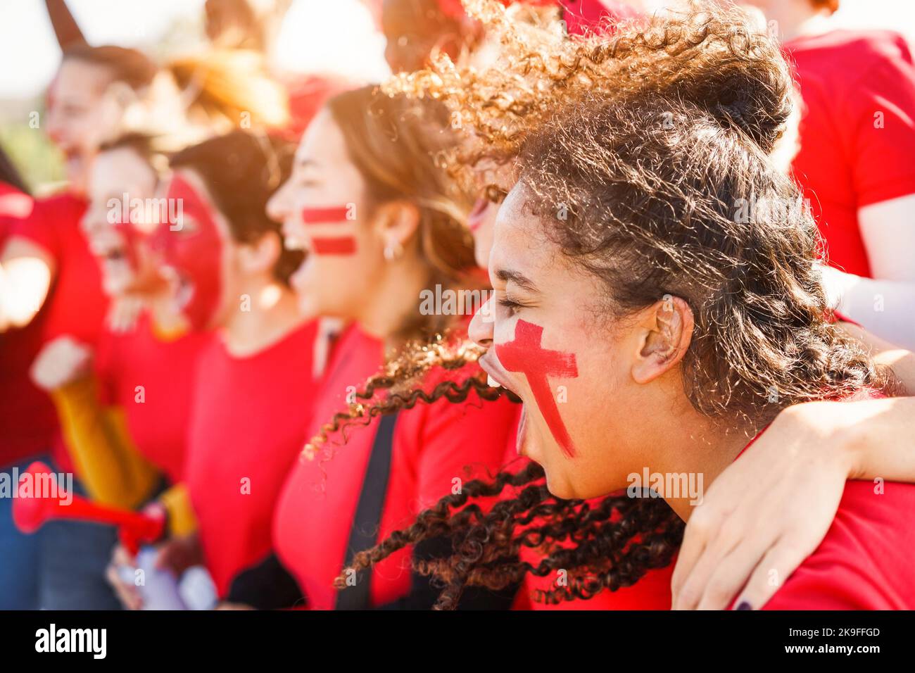 Multiracial red sport fans screaming while supporting their team - Football supporters having fun at competition event - Focus on african girl face Stock Photo