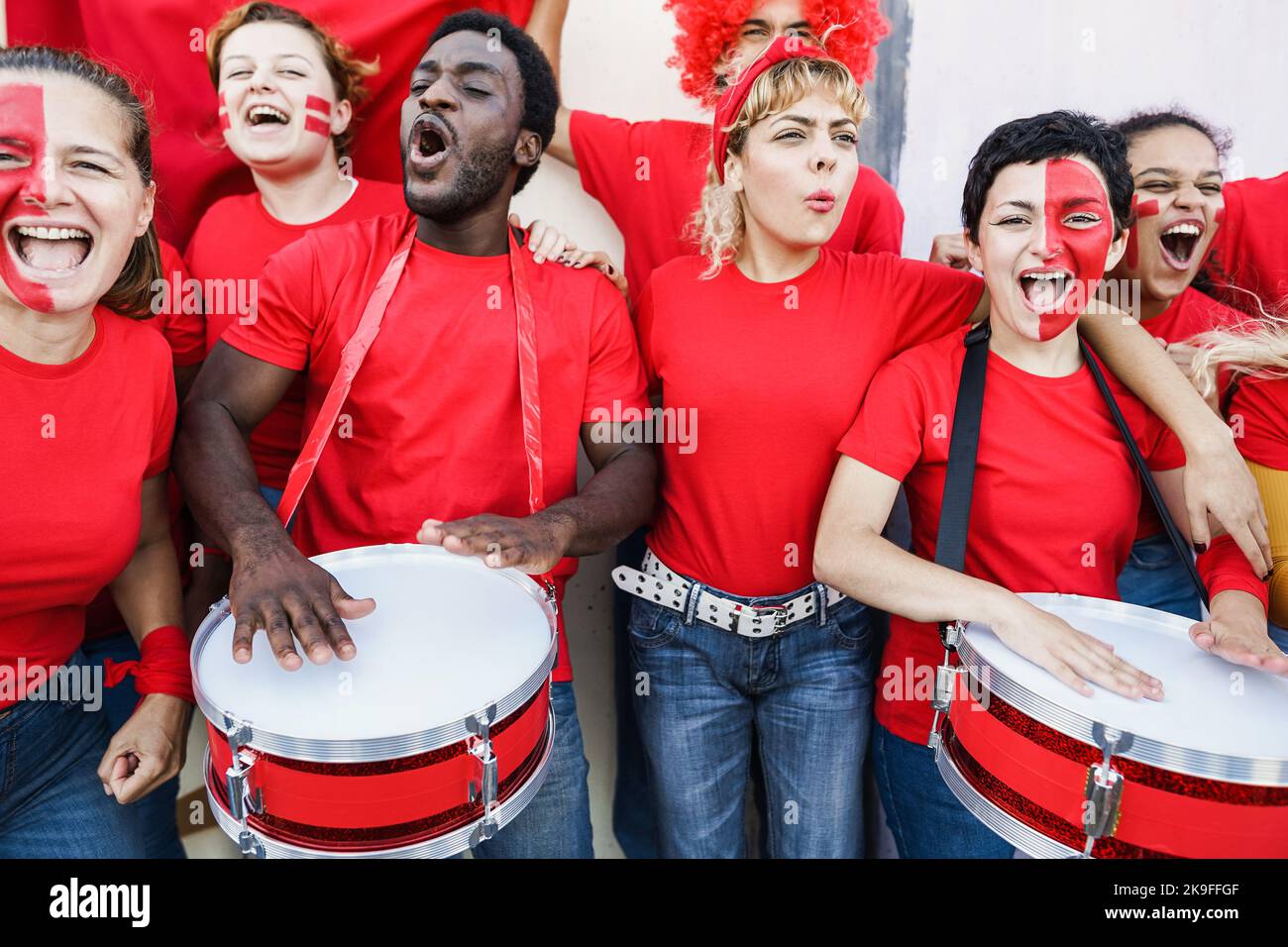 Multiracial red sport fans screaming while supporting their team - Football supporters having fun at competition event - Focus on right girl face Stock Photo