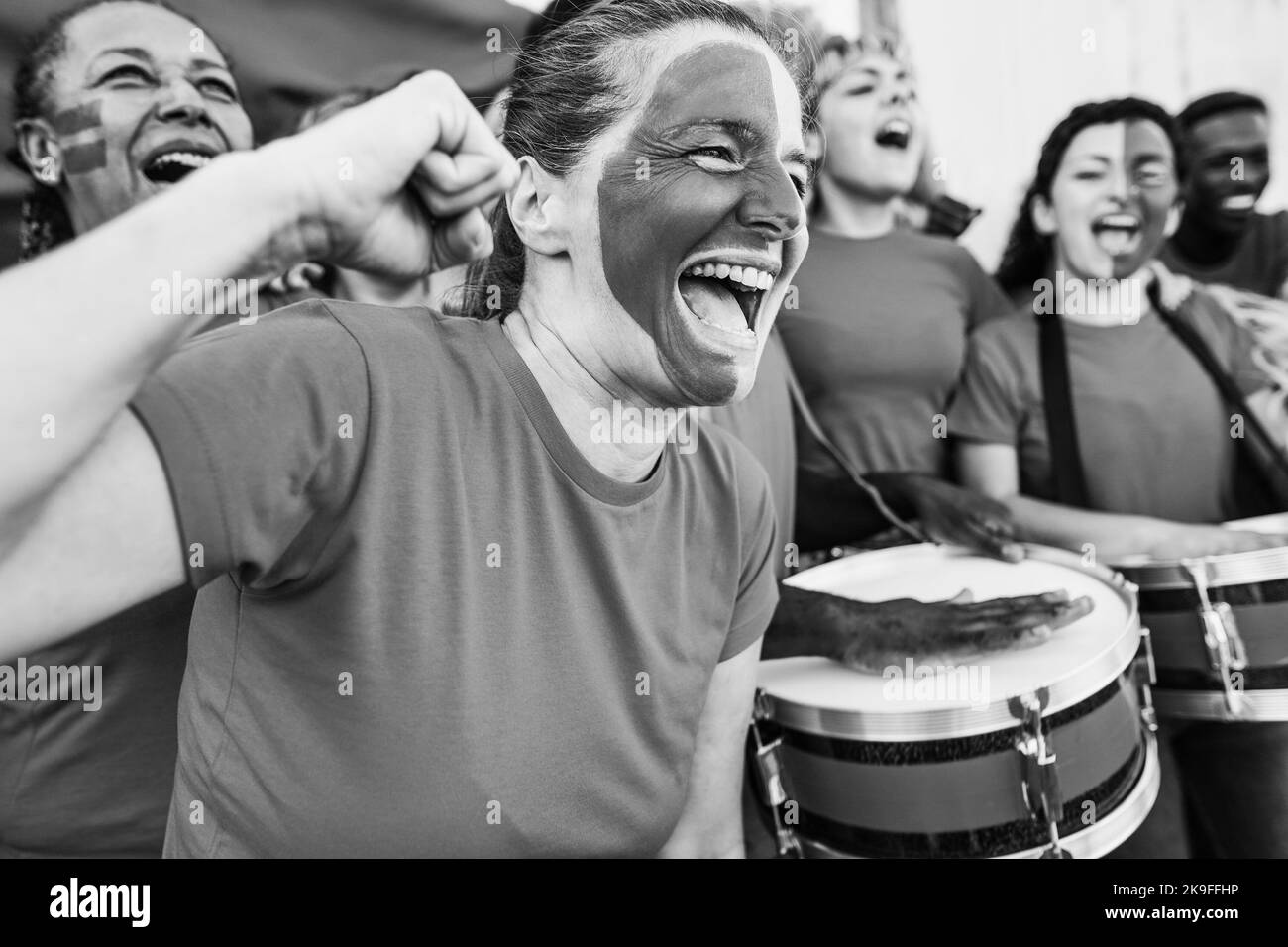 Sport fans screaming while supporting their team - Football supporters having fun at competition event - Focus on mature woman face - Black and white Stock Photo