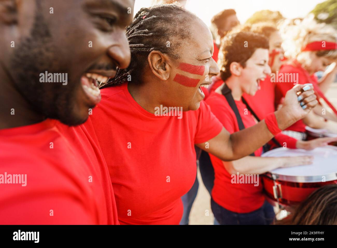 Multiracial red sport fans screaming while supporting their team - Football supporters having fun at competition event - Focus on senior woman face Stock Photo