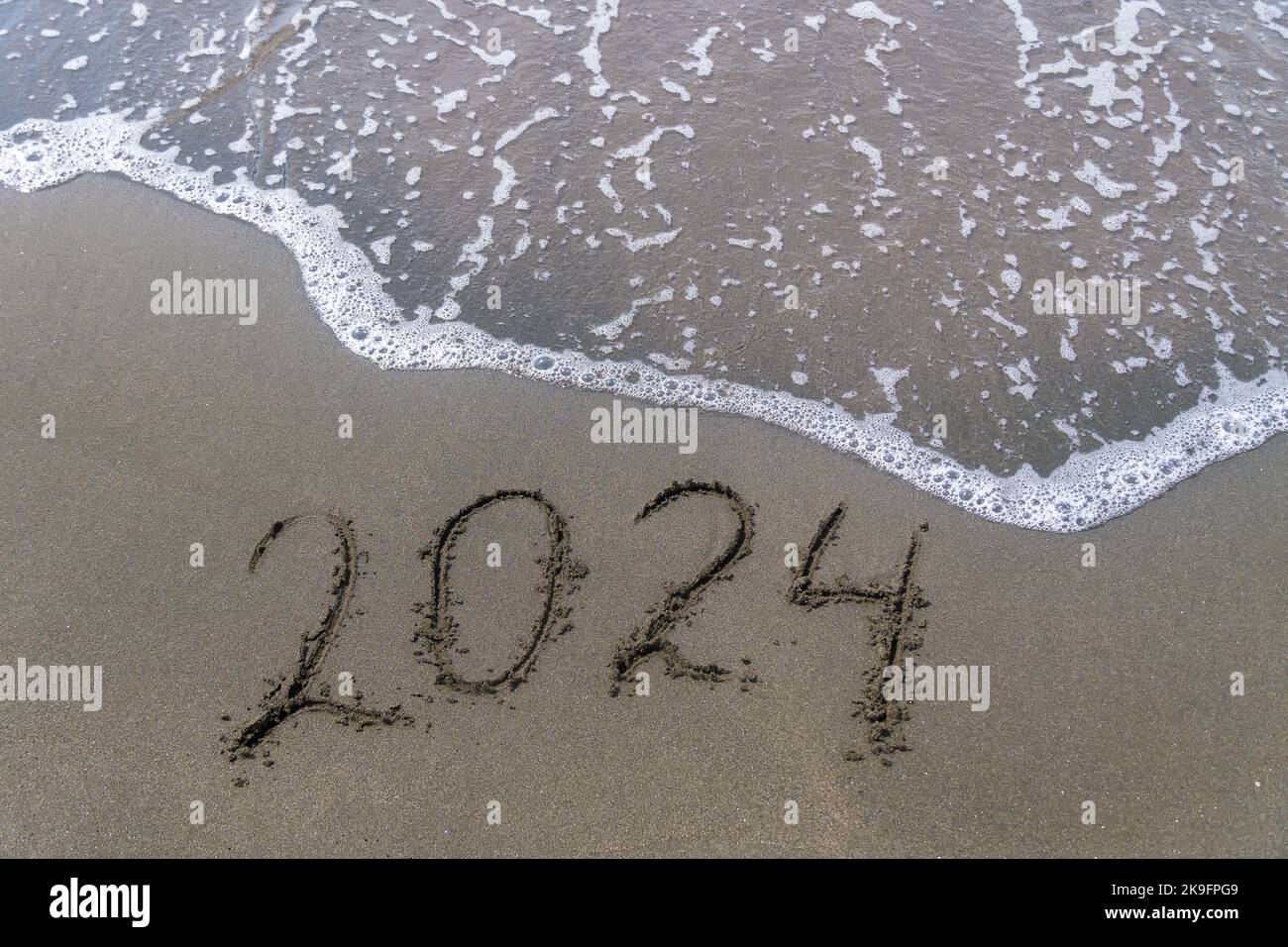 Text Happy New Year 2024 on a sandy sea beach with a small wave
