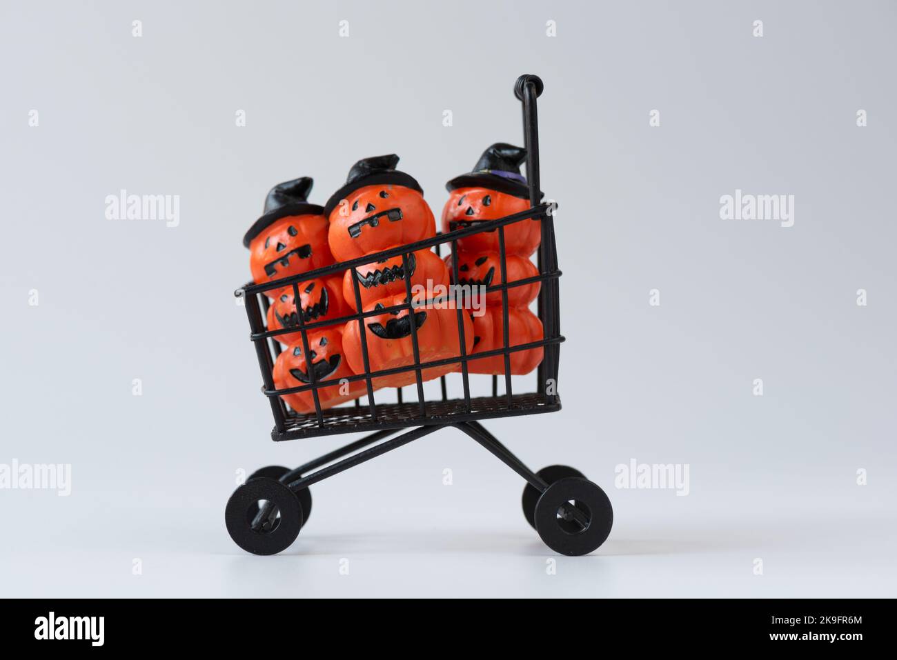 Cute halloween pumpkins wearing hat in shopping cart on white background. Stock Photo