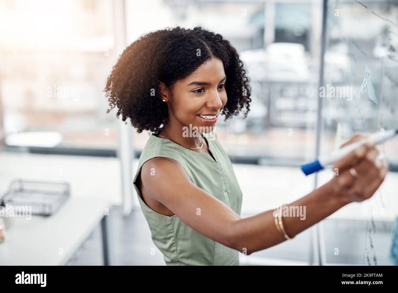 Coming up with a gameplan. an attractive young businesswoman working on a glass wipe board in her office. Stock Photo