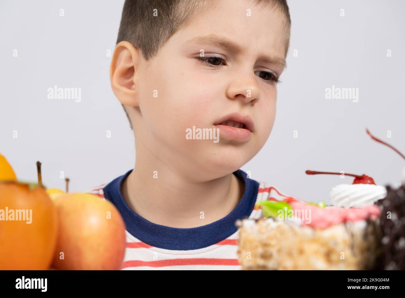 5 year old cute boy sits in front of fruits and cakes and chooses what