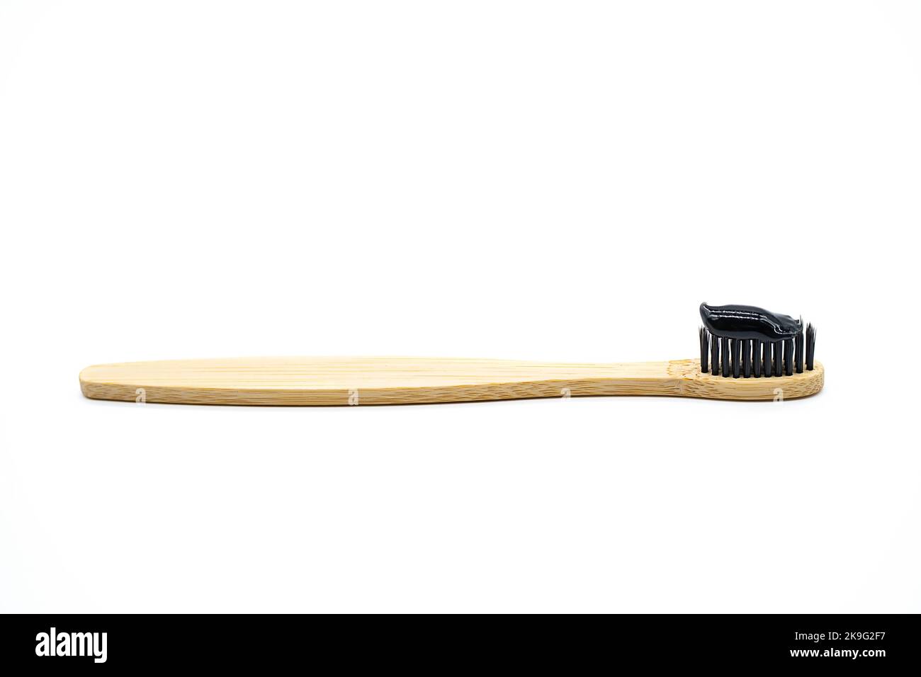 Whitening black charcoal toothpaste on bamboo toothbrush, close up. Eco