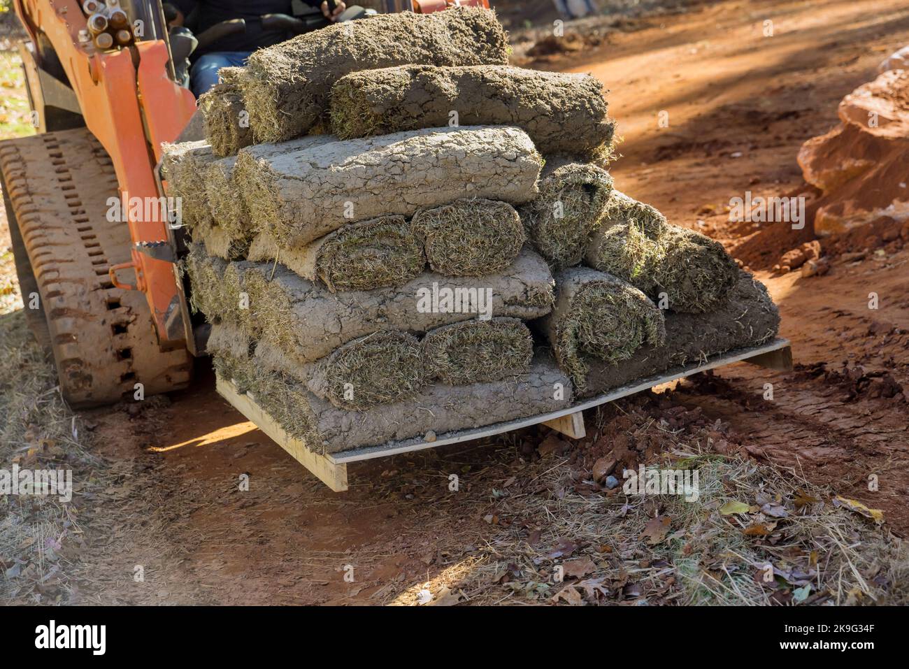 Boom truck unloading green grass turf rolls in pallets for landscaping on construction site with