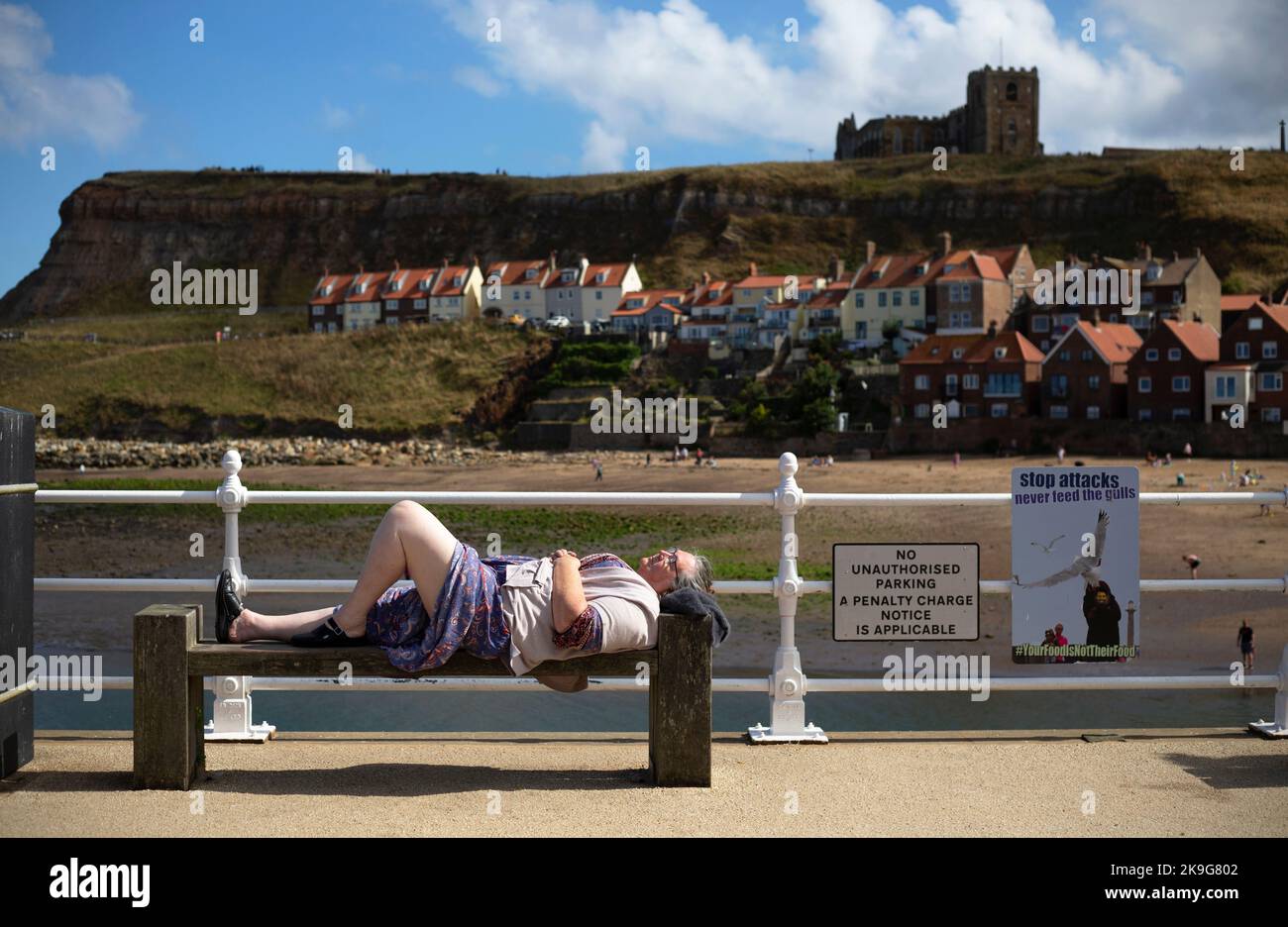 A woman takes a nap on a bench in the seaside town of Whitby in North Yorkshire in Northern England. Stock Photo