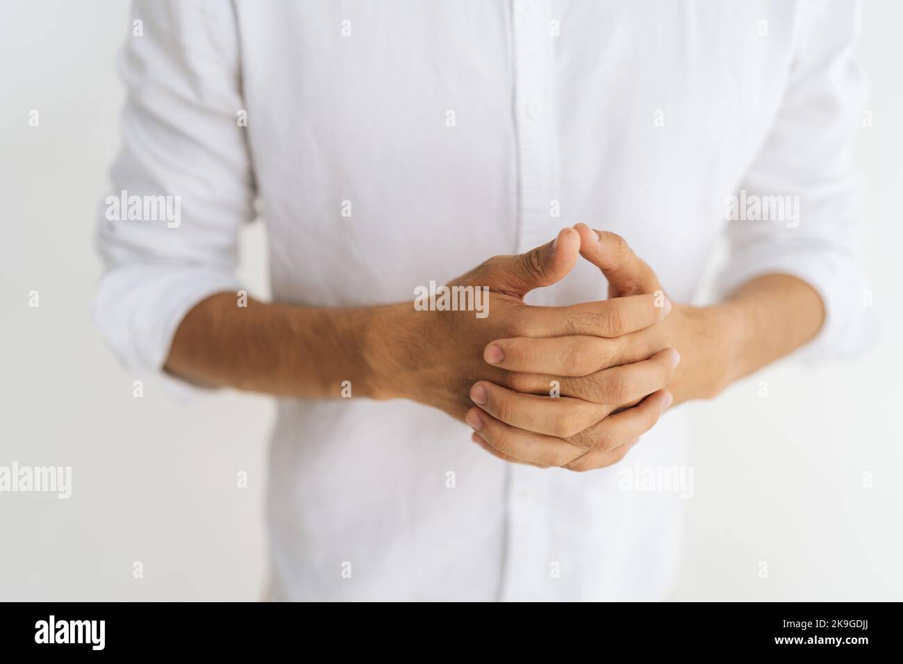 Close-up cropped shot of unrecognizable stressed man ins casual shirt racking knuckles and fingers feeling nervous on white background. Stock Photo