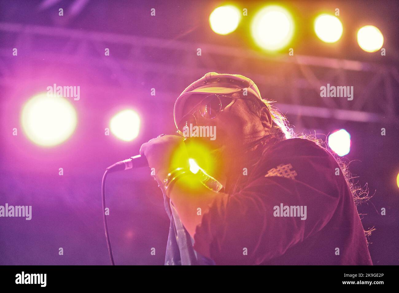 A guy with sunglasses singing on a stage in a blurred colorful lights