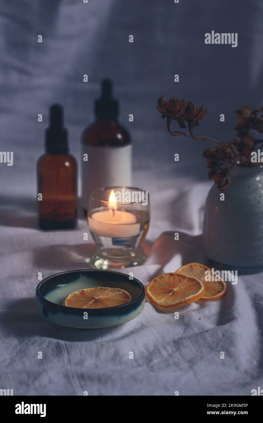 Vertical shot of essential oil bottles, dried lemon slices and a tea candle for a cozy autumn mood spa setting Stock Photo