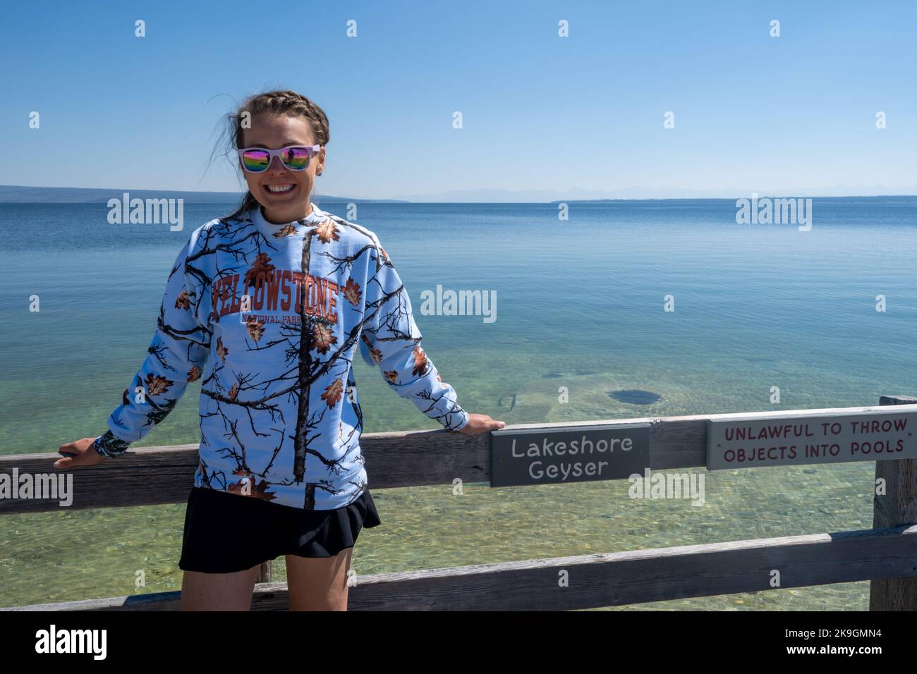 Wyoming, USA - July 19, 2022: Goofy tourist woman wearing a tacky souviner sweatshirt poses at Lakeshore Geyser in Yellowstone National Park Stock Photo
