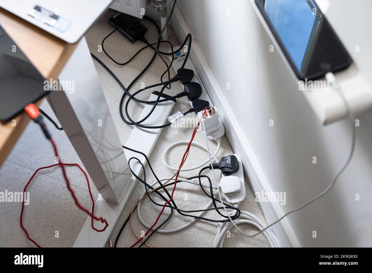 A proliferation of cables from laptop computers, a monitor and smartphones charging, all plugged into an extension adaptor. Working from home, UK Stock Photo