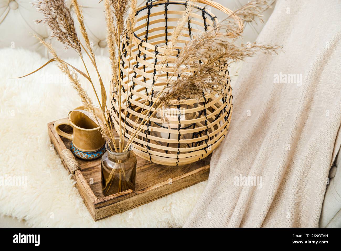 Cozycore or cottagecore concept, warm soft brown beige interior design objects. Cozy wool plaid on sofa, candle burning in wood lantern, tea cup. Stock Photo