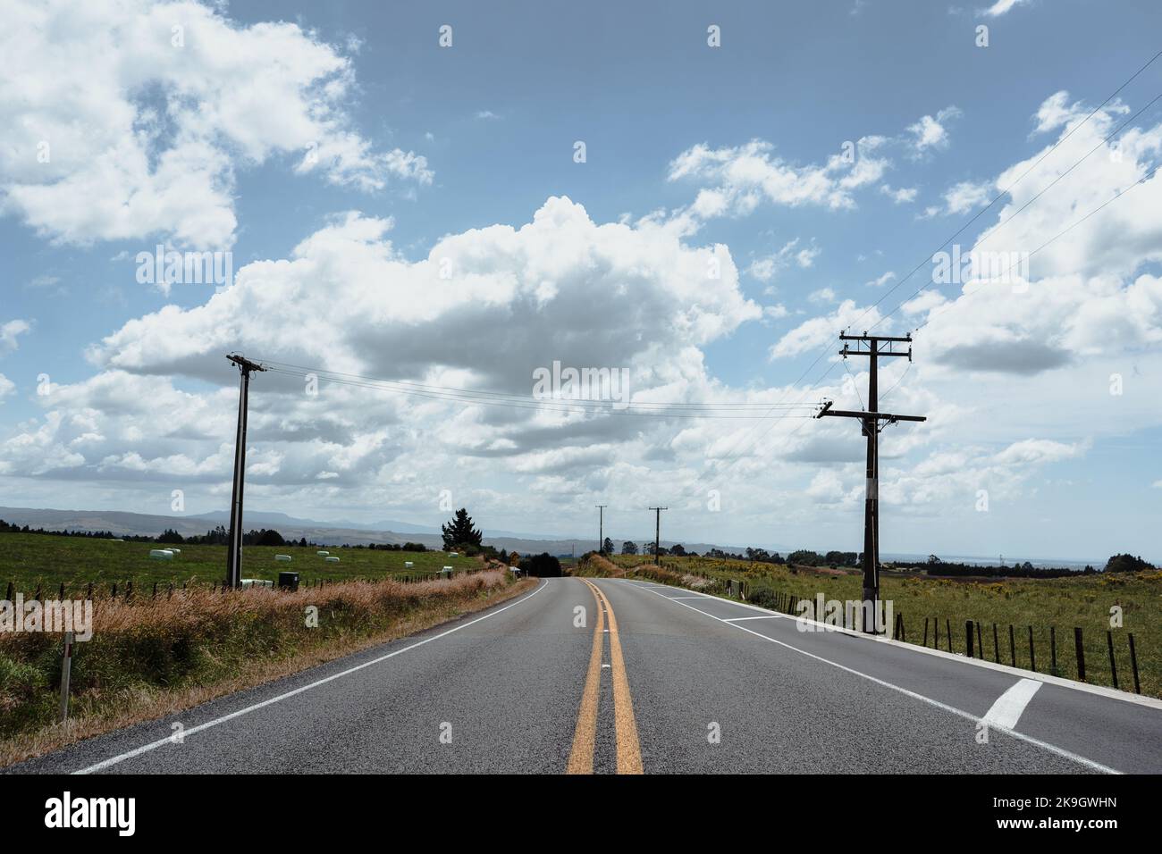 long asphalt road with no traffic next to electricity poles running