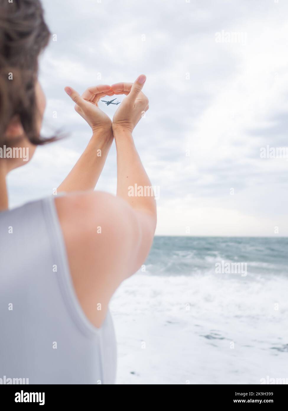 Woman makes heart symbol with flying plane in it. Romantic gesture of wanderlust. Travel by plane concept. Stock Photo