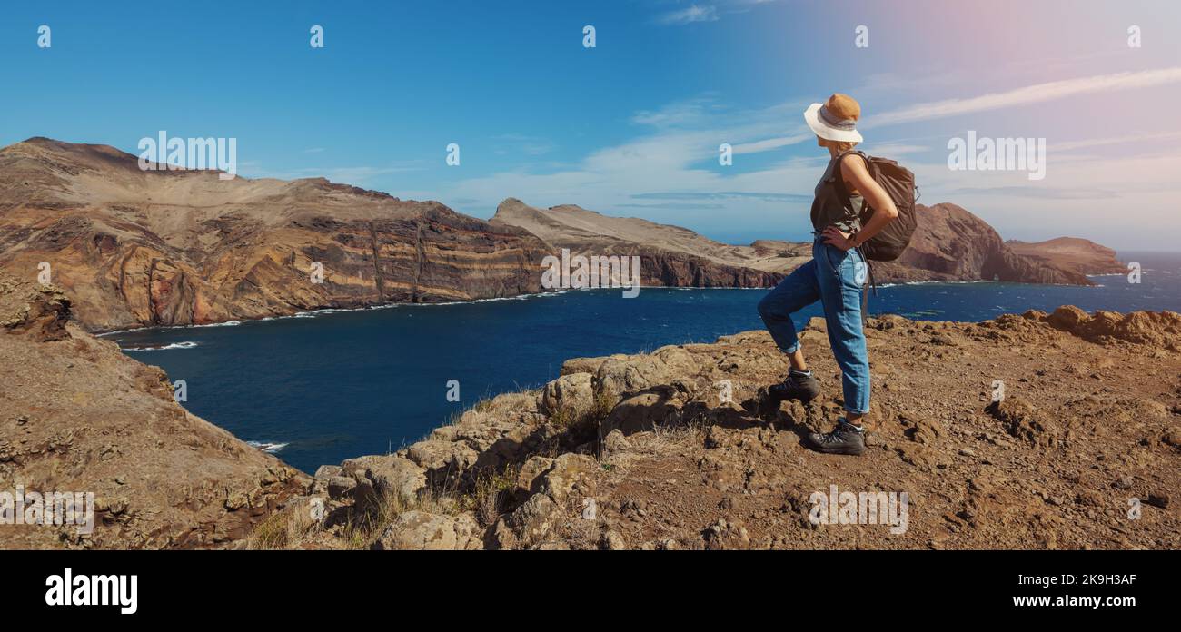woman with backpack standing on cliff and looking to the ocean. mountain trekking and hiking. banner with copy space Stock Photo