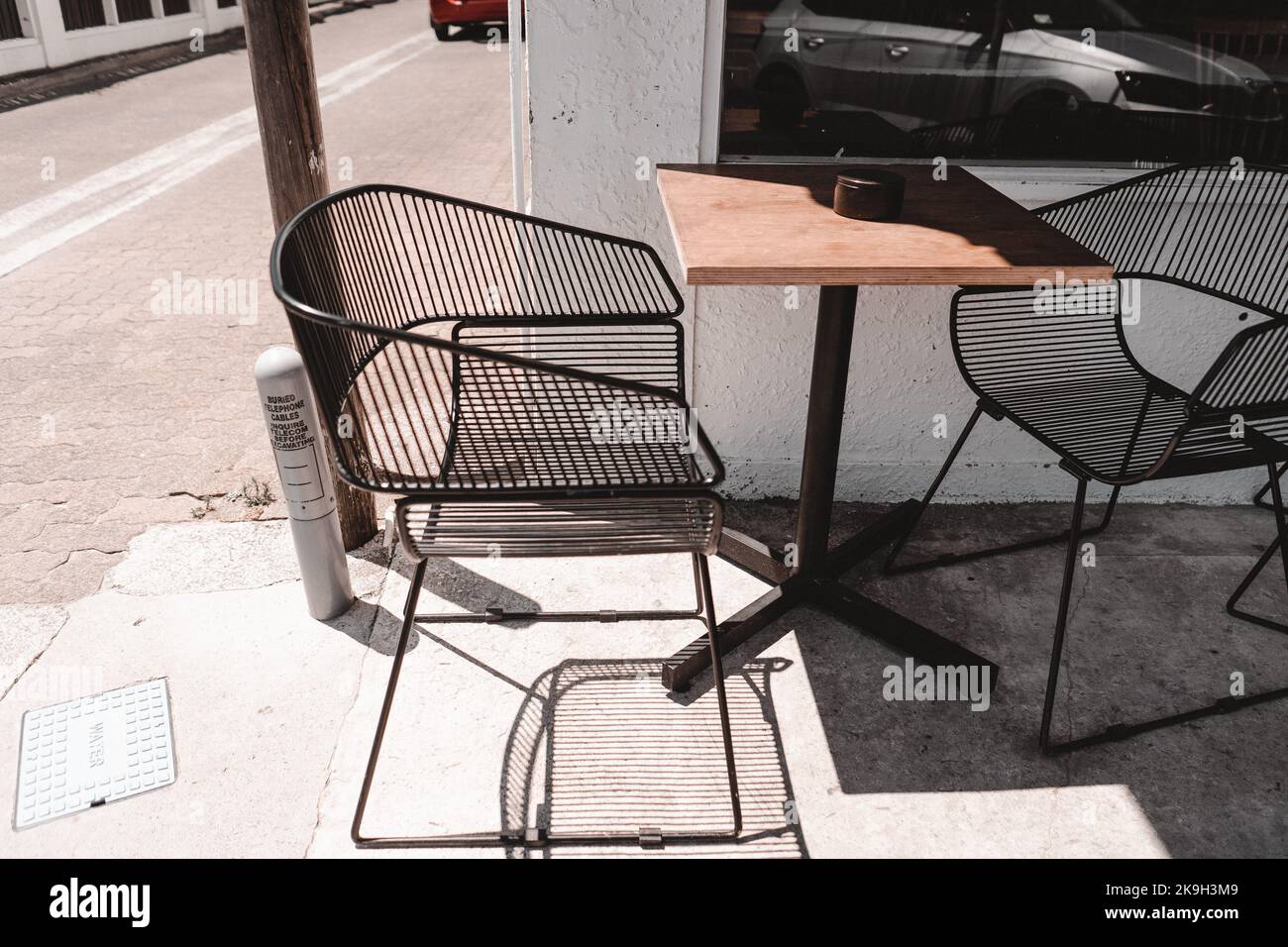Metal wire chairs and wooden table outside a cafe next to sunny corner