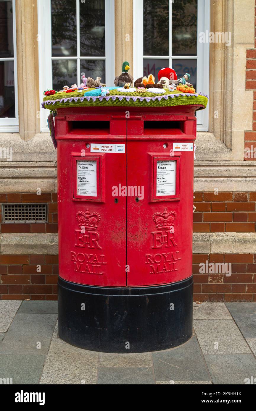Maidenhead, Berkshire, UK. 28th October, 2022. Cheery Autumnal knitted and  crochet post box toppers have appeared on post boxes in Maidenhead High Street. Trees next to the old post office also have crochet scarves and a snake wrapped around them.  Made by 'yarn bombers' they are loved by people young and old. Credit: Maureen McLean/Alamy Live News Stock Photo