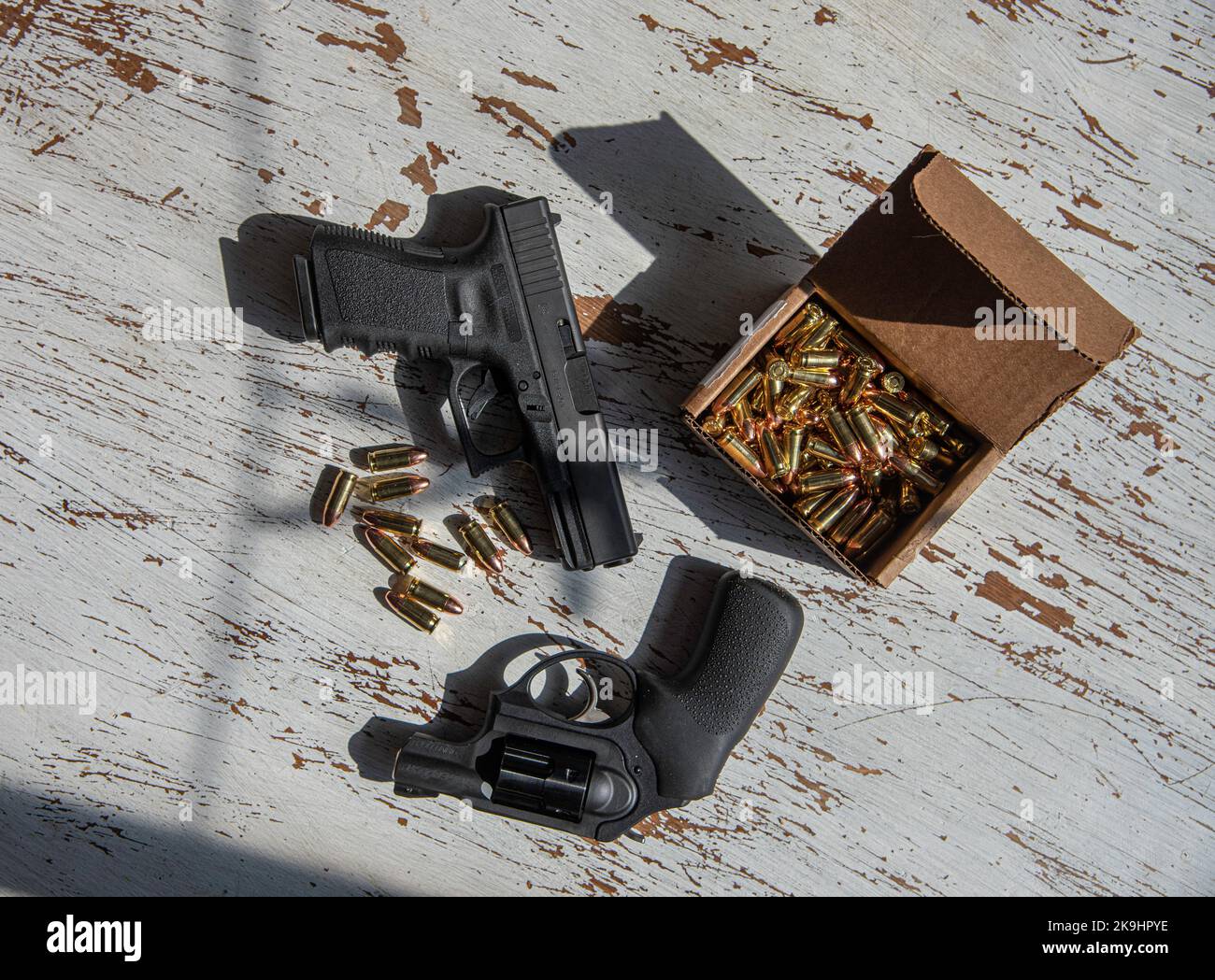 A 9mm Glock pistol and a Ruger 9mm revolver with a box of 9mm ammunition on a table. Stock Photo