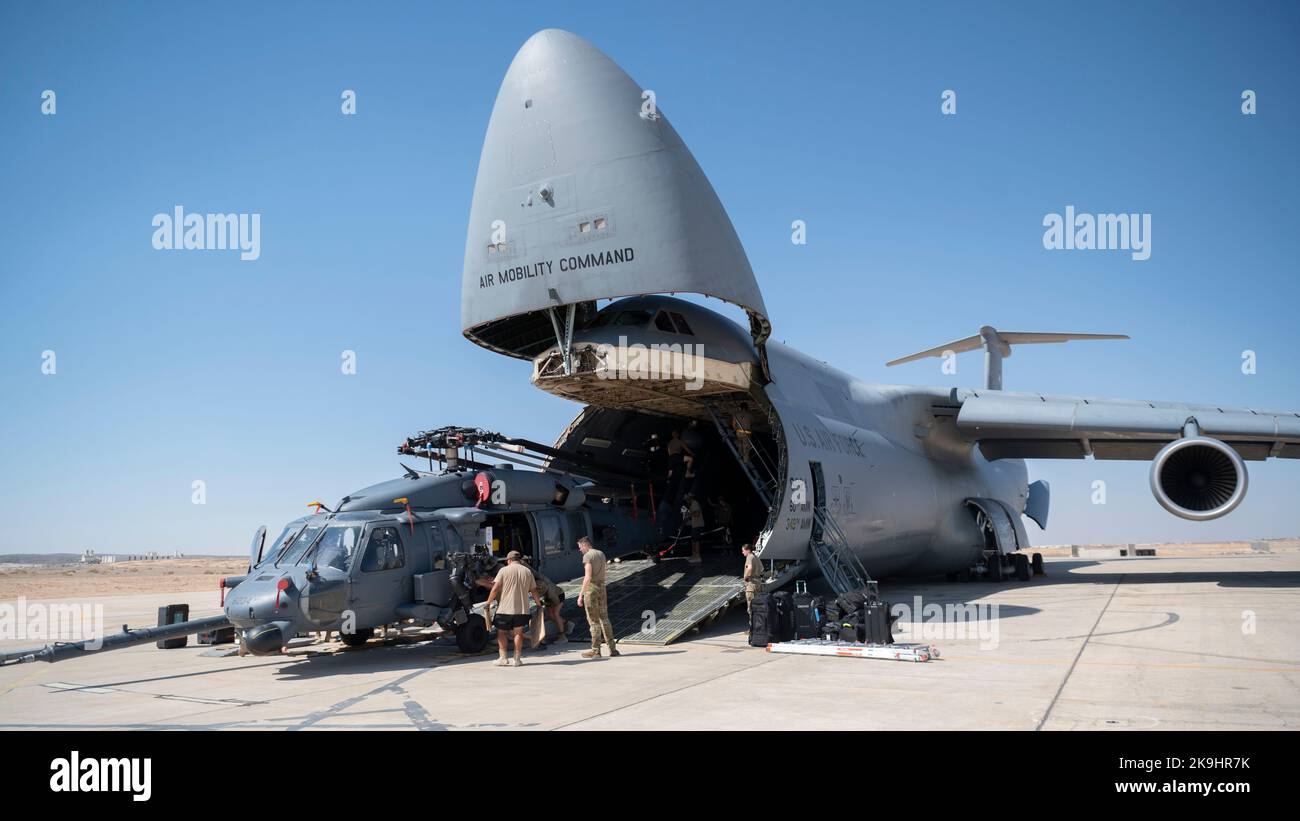 Airmen from the 1st Expeditionary Rescue Group and the 60th Air Mobility Wing, Travis Air Force Base., unload an HH-60 Pave Hawk helicopter along with other cargo from a C-5M Galaxy at an undisclosed location, Southwest Asia, Oct. 11, 2022. The C-5 provides heavy intercontinental-range strategic airlift capabilities and is able to carry oversized loads as one of the largest military aircraft in the world. (U.S. Air Force photo by Tech. Sgt. Jeffery Foster) Stock Photo