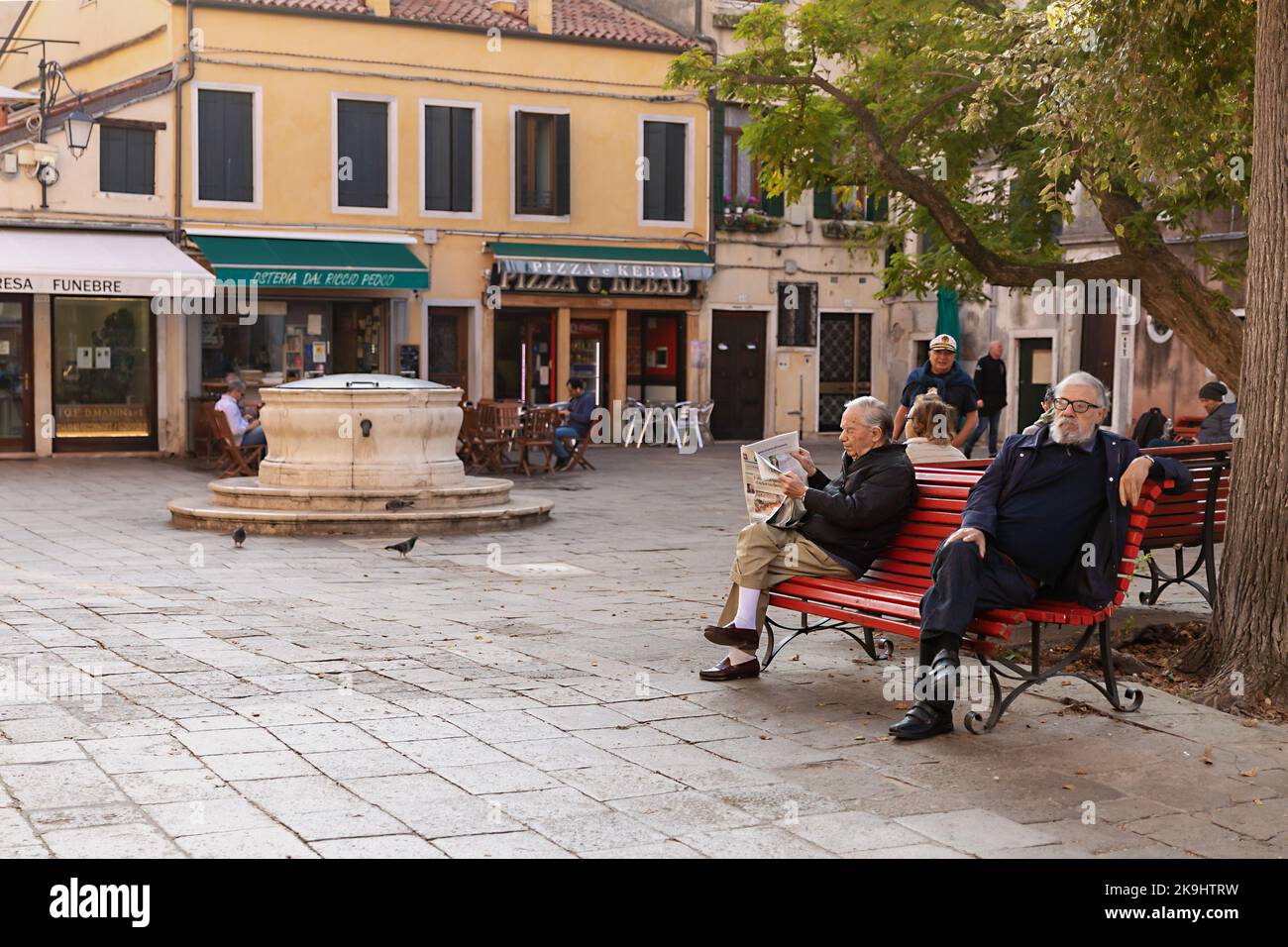 Two local venetians men have rest and read newspaper on the bench in the morning in Venice, Italy Stock Photo