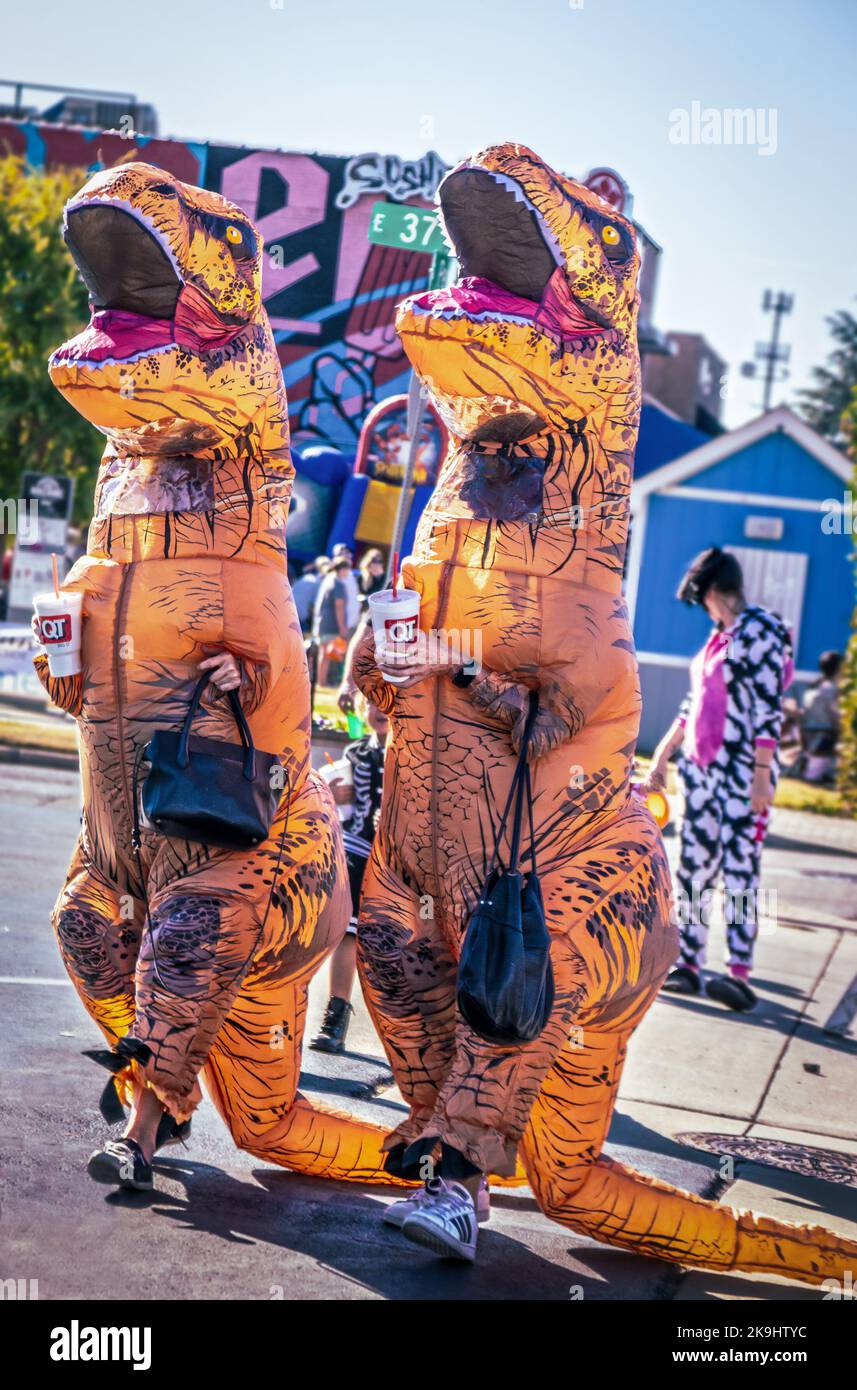 10-22-2022 Tulsa USA - Dinosaurs on the town - Two women in inflatable T-Rex Costumes with handbags and Quick Trip Styrofoam drink cups cross the stre Stock Photo