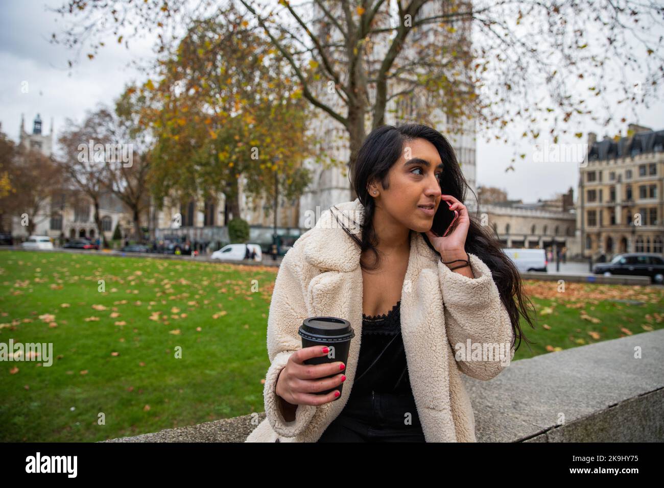 Portrait of a young indian girl chatting on cell phone at a London park during fall Stock Photo