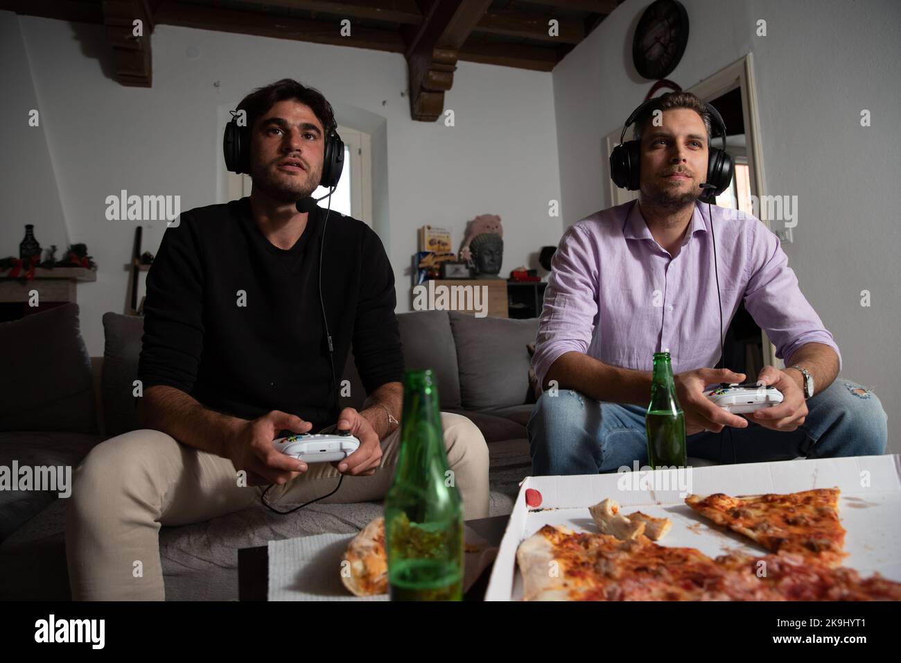 Concentrated friends playing hard and fast at video games with pizza and beer on the table. Stock Photo