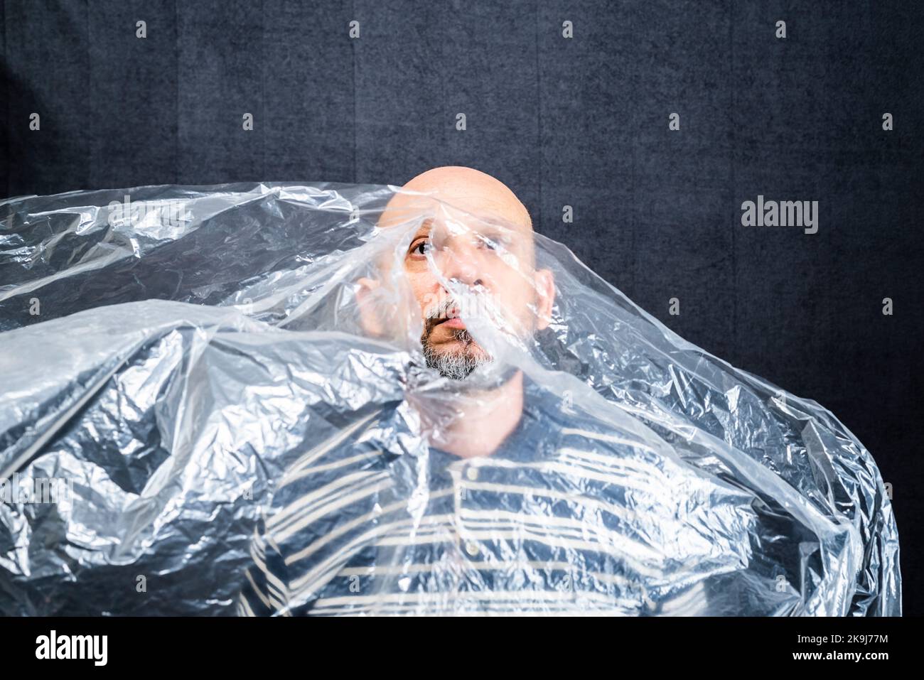 Mature man with a transparent plastic bag flying over his head and face