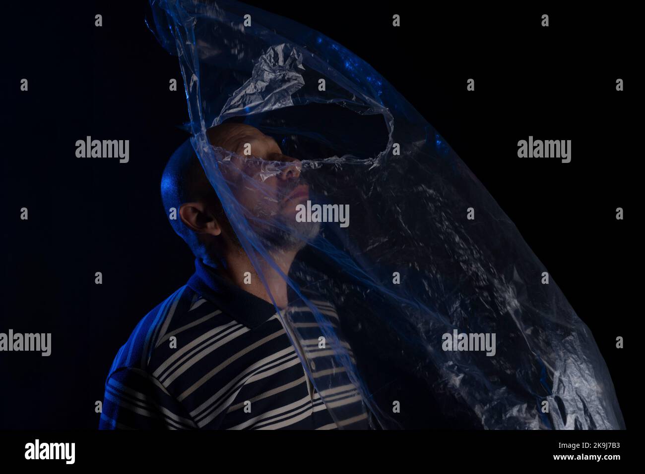 Mature man with a transparent plastic blue bag flying over his head and face. suffocate. face in a plastic bag, strangulation Stock Photo