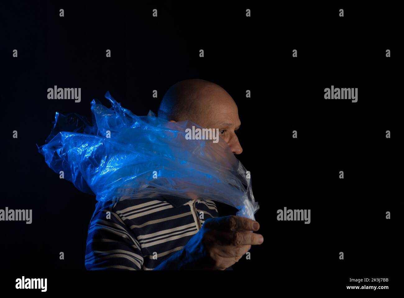 Mature man with a transparent plastic blue bag flying over his head and face. suffocate. face in a plastic bag, strangulation Stock Photo