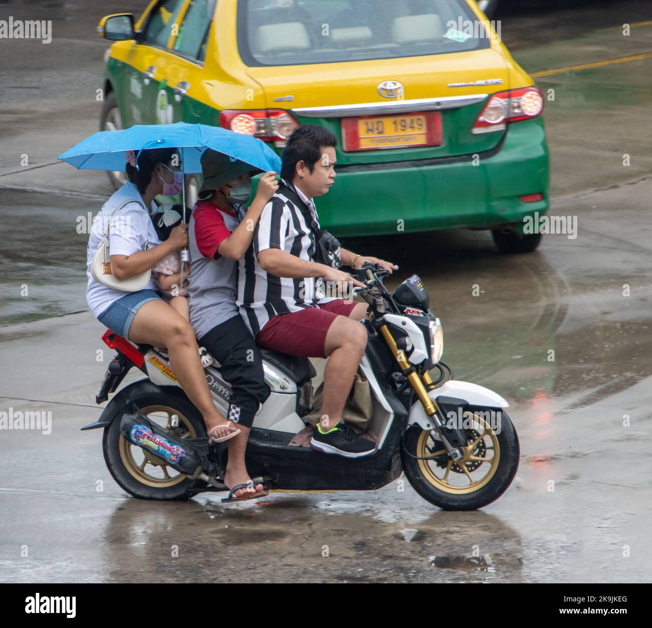SAMUT PRAKAN, THAILAND, OCT 04 2022, A man drives two women hidden under an umbrella on a motorcycle Stock Photo
