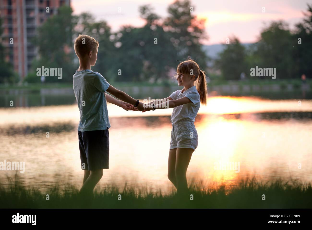 Happy siblings standing together holding hands in summer park. Young children brother and sister relaxing outdoors. Family love and relationship conce Stock Photo