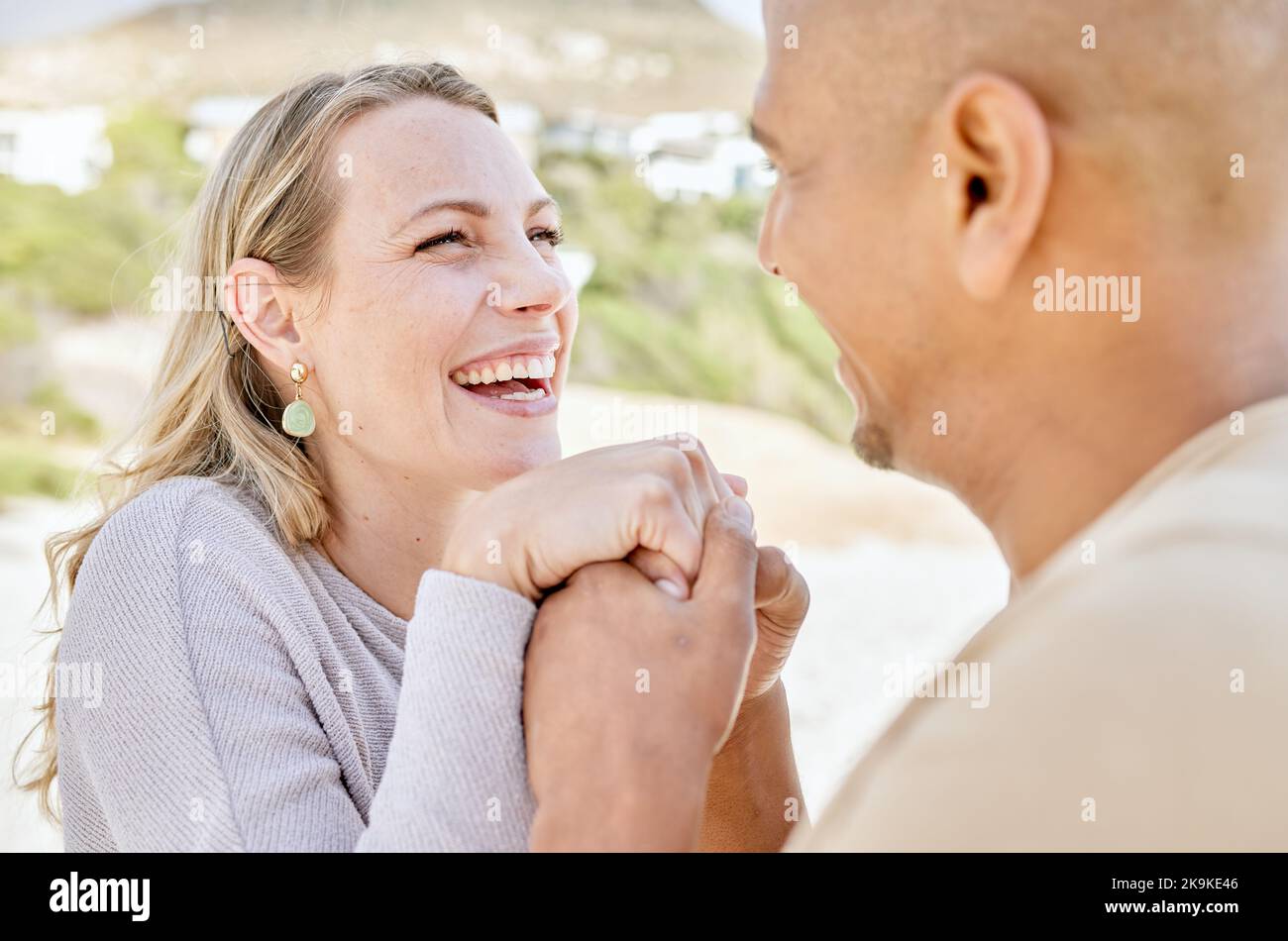 Beach, holding hands and man propose to woman on holiday by sea, happy and smiling together. Affection, romance and multicultural couple by ocean Stock Photo