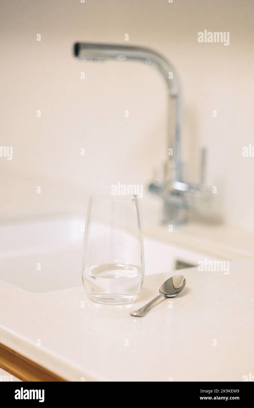 Glass of water and teaspoon on table in kitchen with faucet, closeup. High quality photo Stock Photo