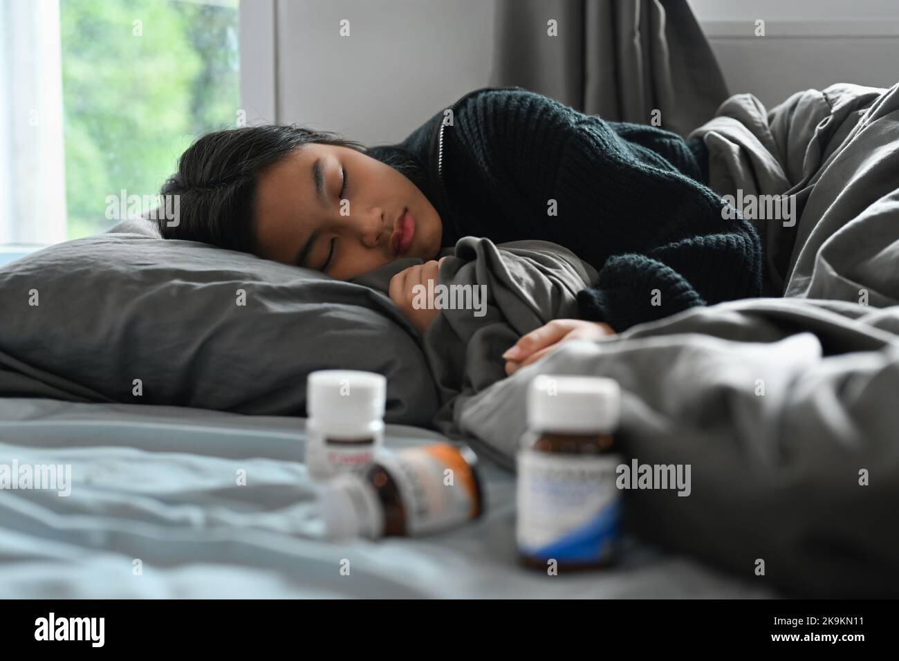 Sick little girl lying in bed under blanket with high fever and flu