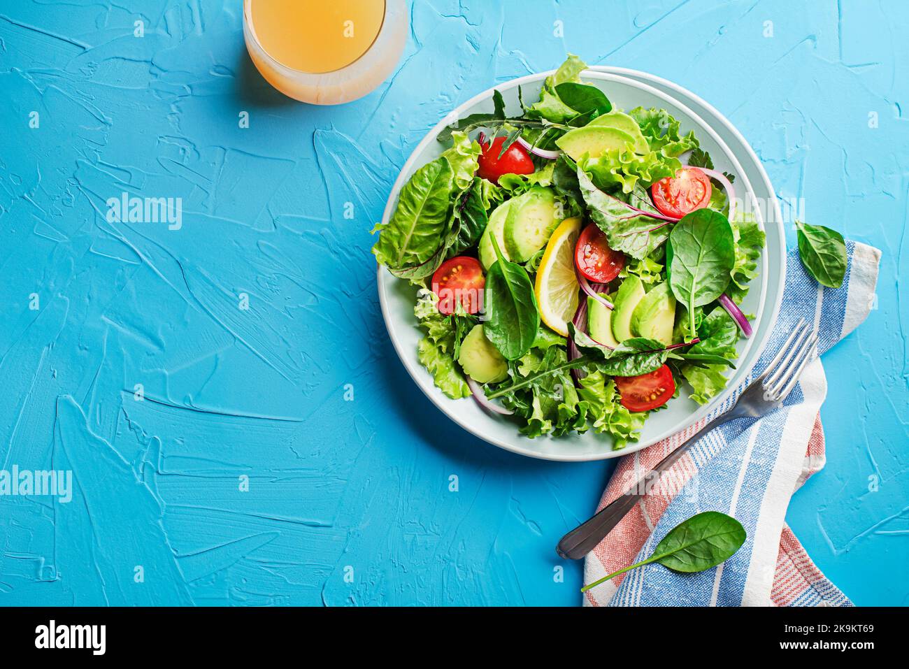 Healthy green salad with avocado and fresh vegetables on blue table close up Stock Photo