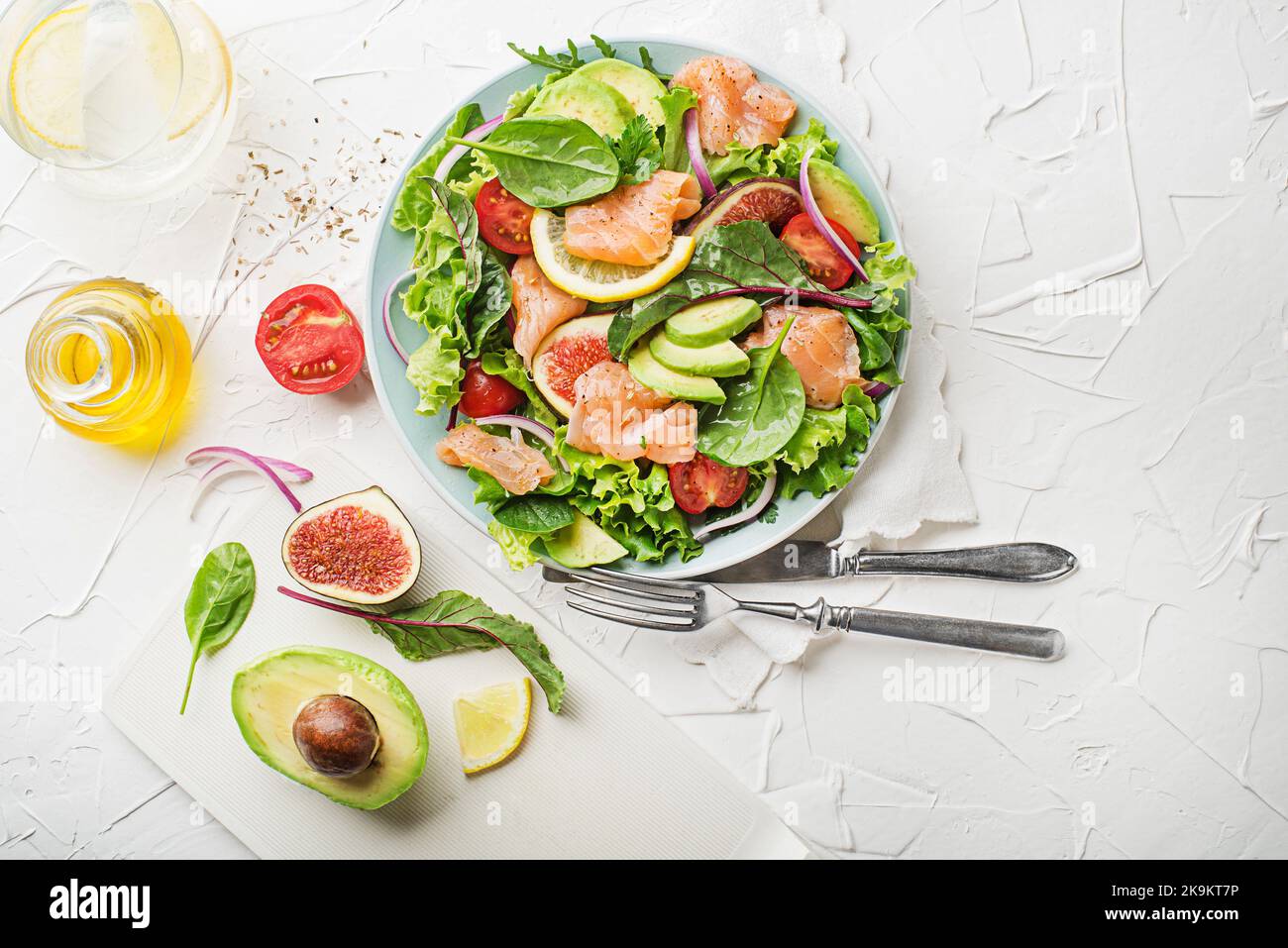 Fresh green salad with smoked salmon, cherry tomatoes, fig and avocado on white table background Stock Photo