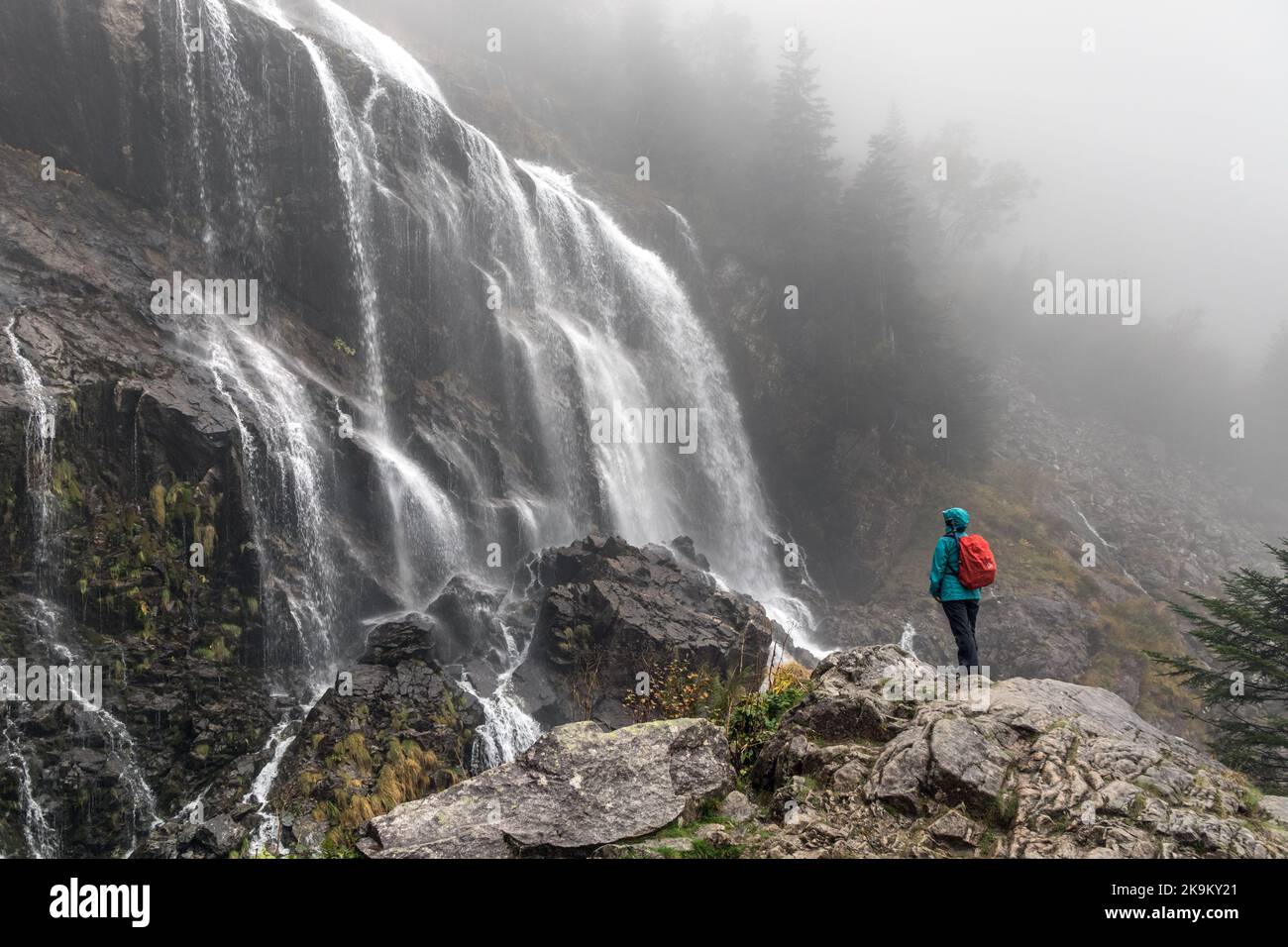 Walker Enjoying a Spectacular view of the Cascade d’Ars in the Rain, Aulus les Bains, Ariege, Pyrenees, France, EU Stock Photo