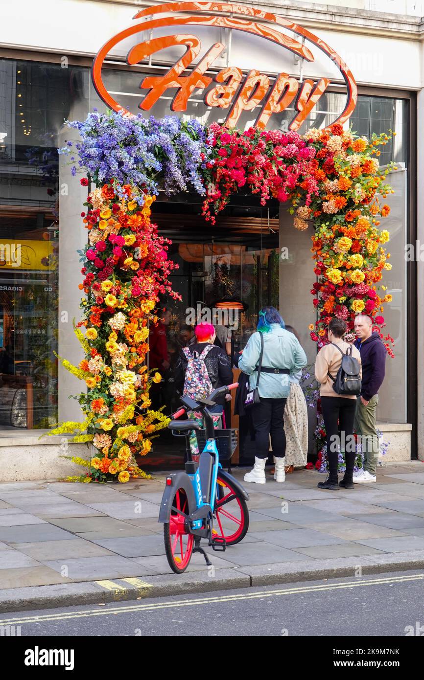 People waiting outside Happy Restaurant, in Piccadilly Circus area of London, with entry decorated with masses of flowers. Stock Photo
