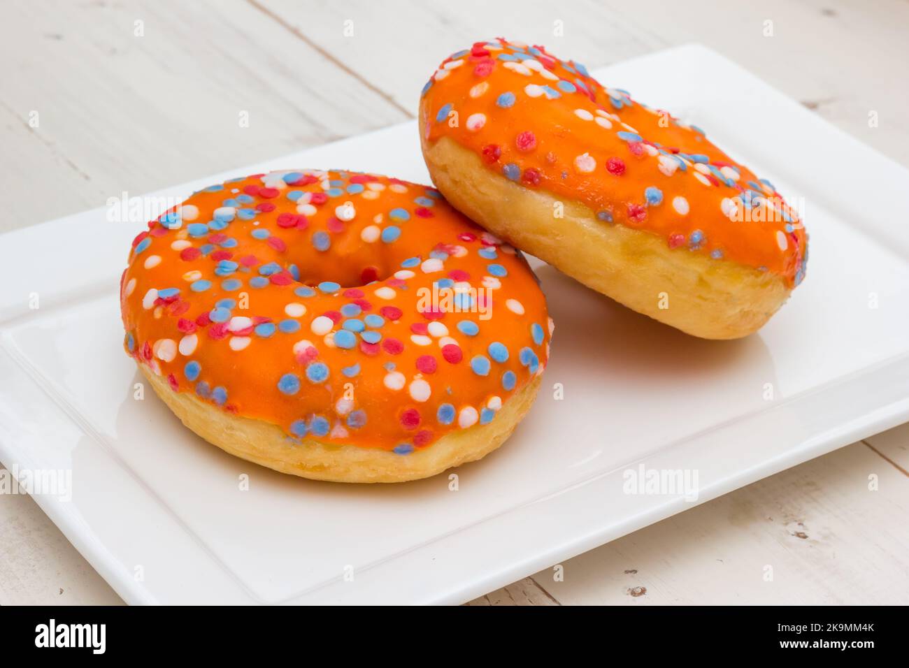 Two orange donuts with sprinkles in the colors of the dutch flag for