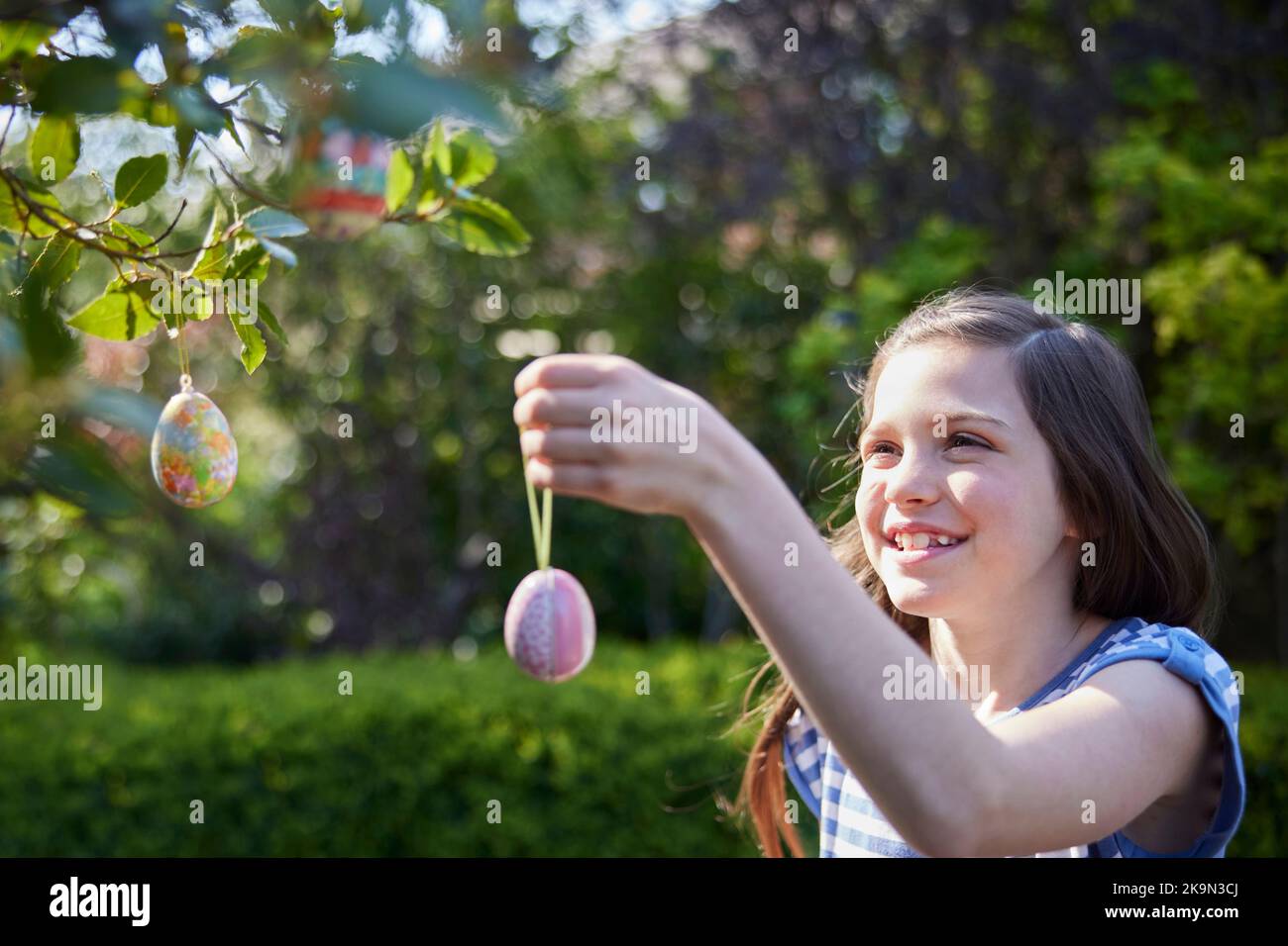 Girl Hanging Homemade Easter Decorations Outdoors On Tree In Garden At Home Stock Photo
