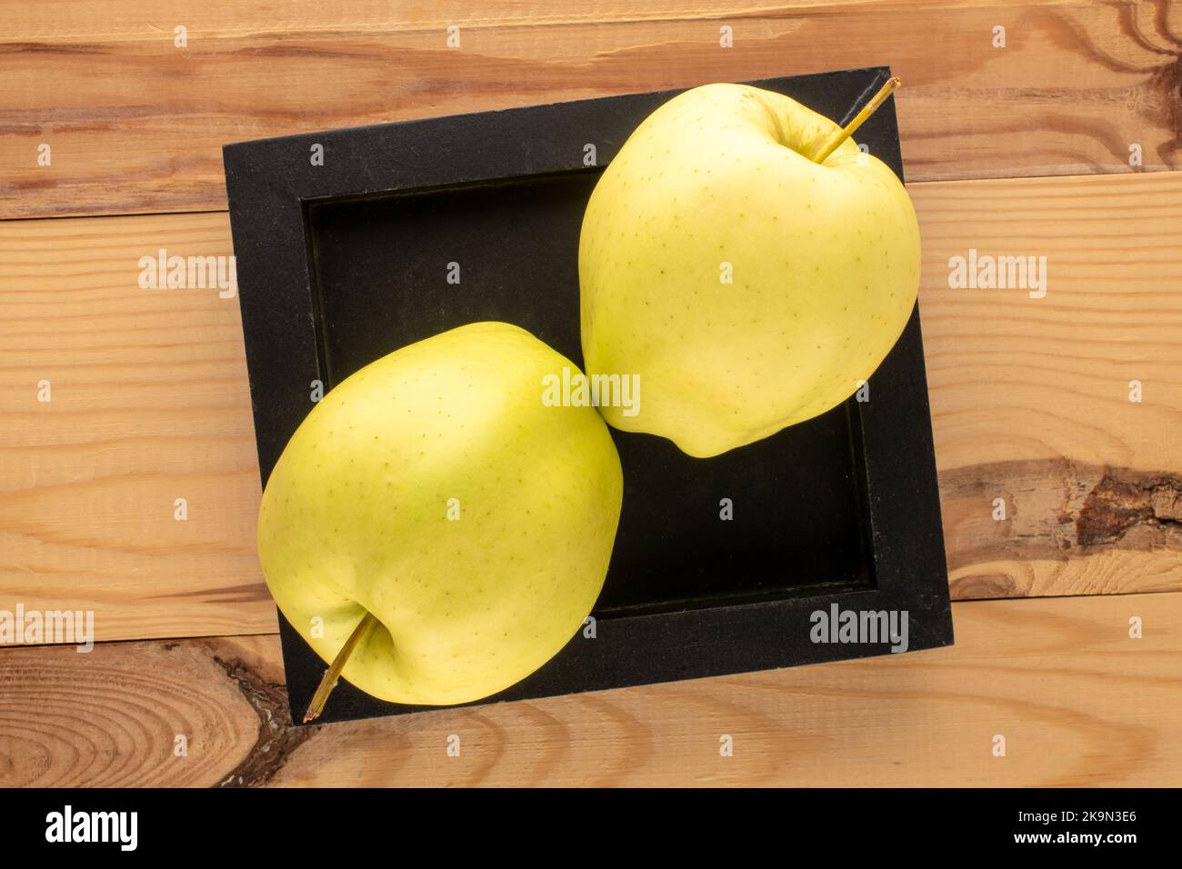 Two Riped Apple Two ripe yellow apples with a wooden plate on a wooden table, macro ...